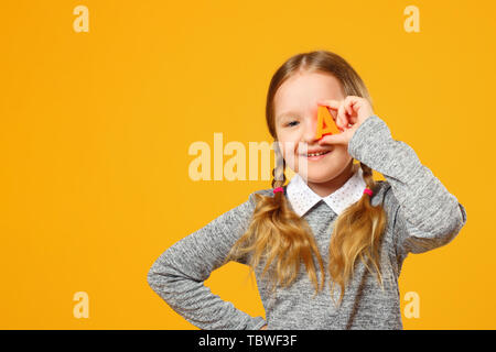 Portrait von Eine fröhliche kleine Kind Mädchen auf einem gelben Hintergrund. Schülerin hält die Buchstaben A. Das Konzept der Ausbildung. Zurück zu Schule. Stockfoto