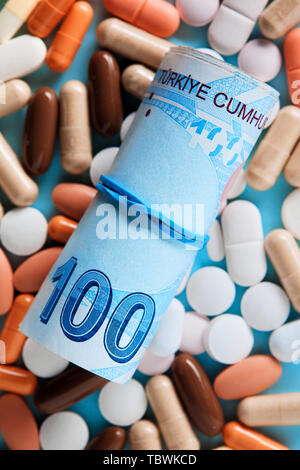 Bis Bündel von hundert Türkische Lira Rechnungen über die medizinische Pillen gerollt. Teure Medizin und Gesundheitswesen Konzept. Overhead Makro anzeigen. Stockfoto