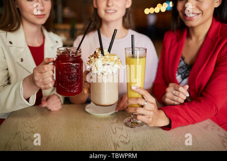 Close-up von lächelnden Frauen an den hölzernen Tisch sitzen und Toasten mit alkoholfreien Cocktails, während Drink zu treffen Stockfoto
