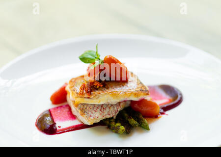 Nahaufnahme einer Pfanne gebratene gegrillter Red Snapper Fischfilet mit Spargel, rote Beete Sauce, Cherry San Marzano Tomaten und Basilikum auf einem weißen Teller natürliche Stockfoto