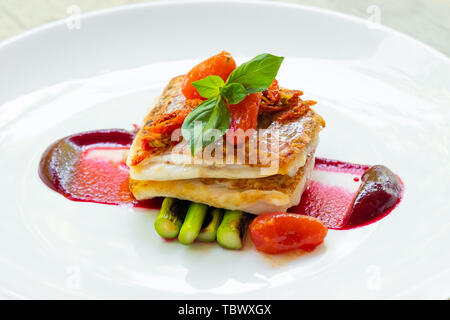 Nahaufnahme einer Pfanne gebratene gegrillter Red Snapper Fischfilet mit Spargel, rote Beete Sauce, Cherry San Marzano Tomaten und Basilikum auf einem weißen Teller natürliche Stockfoto