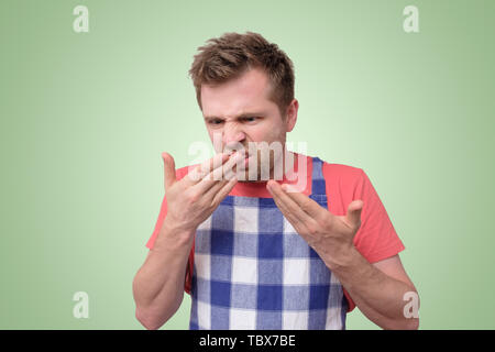 Missfallen junger Mann in Schürze sniffing seine Hände. Stockfoto