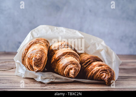 Drei köstliche Croissants in Backpapier auf hölzernen Tisch gewickelt. Close-up. Stockfoto