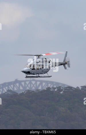 Der Royal Australian Navy (RAN) Bell 429 Helikopter N 49-048 fliegen über den Hafen von Sydney mit der Sydney Harbour Bridge im Hintergrund. Stockfoto