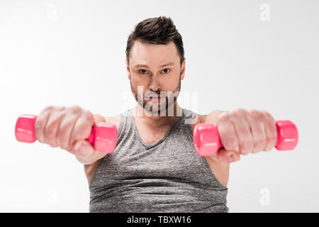 Übergewicht Mann an der Kamera schaut während der Arbeit aus mit rosa Hanteln isoliert auf weißem Stockfoto