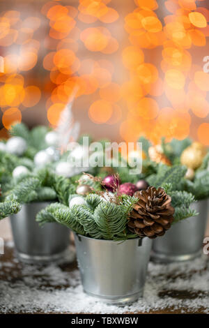 Schöne festliche eingestellt. Kleine Arrangements von frischem Fichtenholz, rosa Zierpflanzen in einem rustikalen hölzernen Kasten. Weihnachtliche Stimmung. Girlande bokeh für den Hintergrund. Bokeh Stockfoto