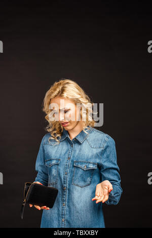 Verärgert blonde Frau mit Blick auf leere Mappe und gestikulierend auf Schwarz isoliert Stockfoto