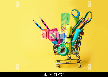 Zurück Konzept mit Warenkorb und Bunte Bleistifte zur Schule, Quadrat Lineal, Schere, Clips, Markierungen auf Pastellgelb Kulisse. Flach, Ansicht von oben, Stockfoto
