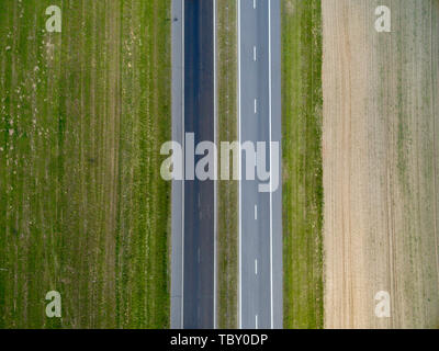 Antenne Blick von oben auf die asphaltierte Straße durch ein grünes Feld im Sommer in Belarus. Natur aus der Vogelperspektive Stockfoto