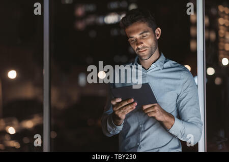 Junge Unternehmer mit einem Tablet in seinem Büro in der Nacht Stockfoto