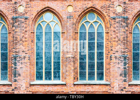 Hohe Fenster mit Spitzbögen auf dem Hintergrund der alten Mauer aus rotem Backstein. Vom Fenster aus der Serie der Welt. Stockfoto