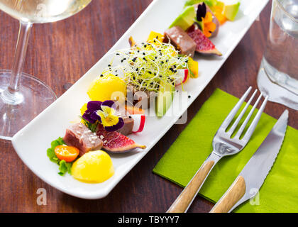 Teller mit leckeren gebratenen Thunfisch mit Mango, Avocado und Feigen auf lange Platte serviert. Stockfoto