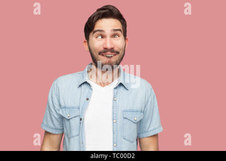 Portrait von Crazy gut aussehender bärtiger junger Mann in blau casual style Hemd mit gekreuzte Augen und suchen mit lustigen Komiker Gesicht. indoor Studio Stockfoto