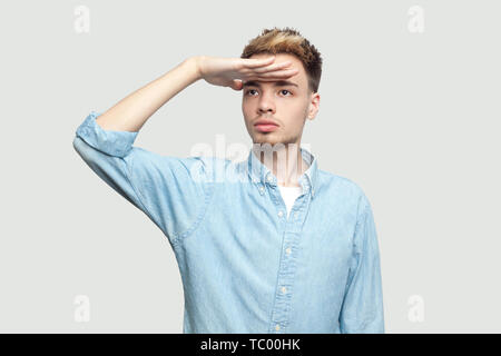 Porträt von Ernst aufmerksam hübscher junger Mann in Hellblau shirt stehend mit der Hand auf die Stirn und Wegsehen mit ernsten Gesicht. indoor Studio Stockfoto