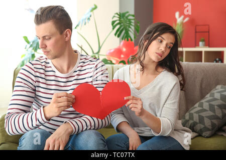 Unglückliche junge Paar zerreißt Papier Herzen zu Hause. Konflikt in Beziehung Stockfoto