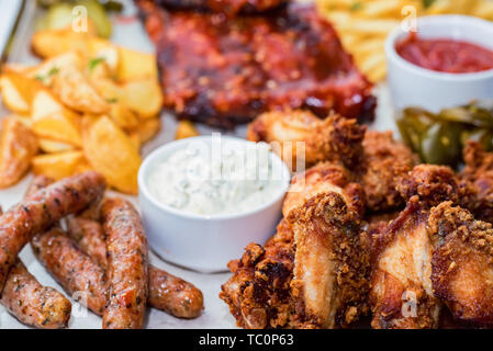 Schüssel gemischter Aufschnitt. Gegrillte Spareribs, Chicken Wings und Würstchen mit Pommes frites Stockfoto