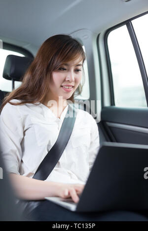 Schöne asiatische junge Frau mit Laptop im Auto. Stockfoto