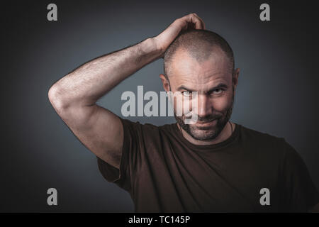 Porträt eines Mannes, der seinen Kopf kratzen mit einem nachdenklichen Ausdruck. Direkter Blick in die Kamera. Legere Kleidung studio shot Bild. Stockfoto