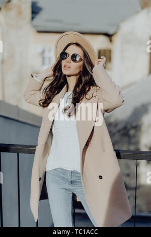 Outdoor Portrait von junge Schöne modische Frau in Street posieren. Modell tragen stilvollen grauen Mantel, Hut, weiße runde Sonnenbrille. Weibliche Mode c Stockfoto