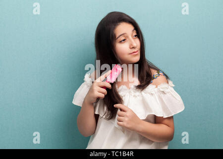 Portrait von gesunden schönen Teenager brunette Mädchen in weißem Kleid und Kämmen brünette Haare mit rosa Haarbürste. Morgen kümmern. Indoor, isol Stockfoto