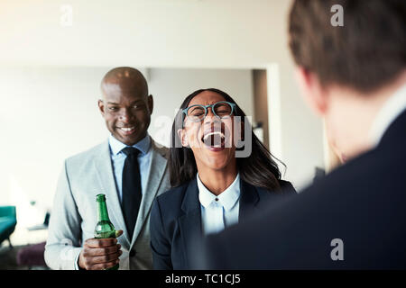 Junge afrikanische amerikanische Geschäftsfrau Lachen schwer, während Drinks mit Kollegen im Büro nach der Arbeit Stockfoto