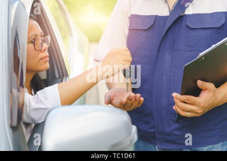 Asiatische Frau im gebrochenen Auto sitzen die Schlüssel der Automechaniker für Wartungsarbeiten in der Garage. Sonnenlicht und flare Hintergrund Konzept. Stockfoto