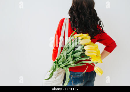 Junge Frau mit gelben Blüten in Leinen eco Beutel auf Schulter. Das Drehen um auf einem leuchtend weißen Hintergrund Stockfoto