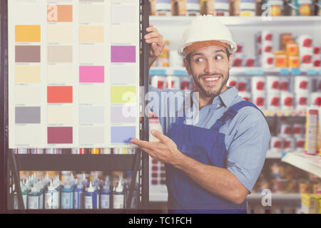 Junge Meister in blauen Overalls mit Proben von Farbe auf Stand in Store Stockfoto