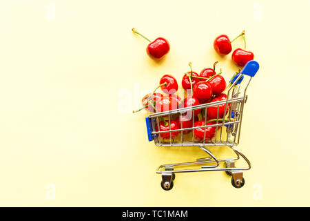 Mini shopping Lebensmittelgeschäftkarre voller Frische Kirschen. Frische Beeren auf gelben Hintergrund. Gesunde, Sommer essen Konzept. Für text Stockfoto
