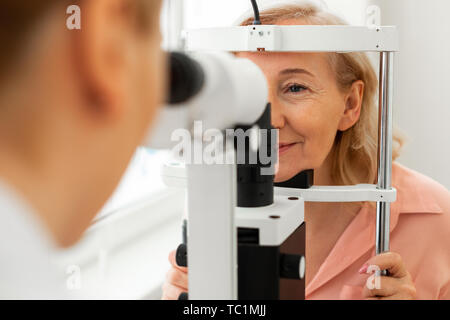 Strahlende zufriedene Frau. Fleißige ruhige Frau genau ihr Gesicht in speziellen Rahmen beim Arzt Augen aus der Nähe beobachten Stockfoto