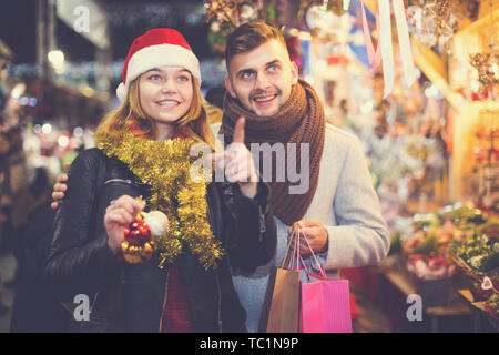 Freudige junge Paar in hat die Wahl Dekoration zu Weihnachten Fair, Mädchen Punkte zu den Dekorationen Stockfoto