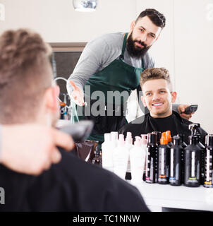 Positiven erwachsenen mann Friseur angezeigte Ergebnis der Arbeit zu den glücklichen Kunden im Friseursalon Stockfoto