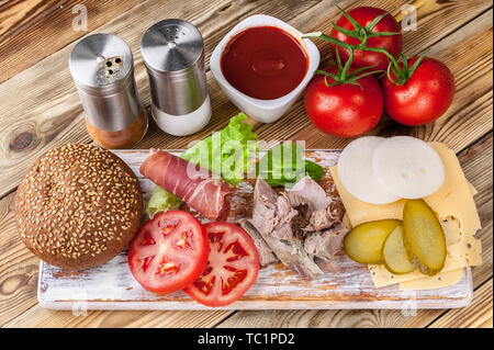 Fleisch, Käse, Tomaten, Zwiebeln, Gurken, Salat, Sauce, Gewürze und Speck. Hamburger Zutaten. Stockfoto