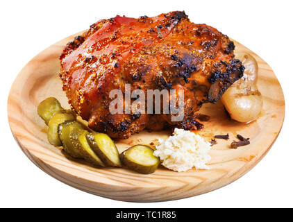 Leckere Schweinshaxe mit knuspriger Kruste geschmort in Bier auf Holzplatte mit Gurken serviert. Auf weissem Hintergrund Stockfoto