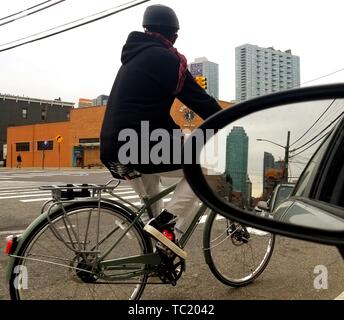 Ein Radfahrer Fahrten durch Verkehr in Long Island City, Queens, New York, mit einer Linie der Autos und der Citigroup Gebäude spiegeln sich in einer Rückspiegel, 29. März 2019. () Stockfoto