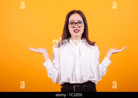 Junger Teenager Mädchen mit den Händen in der Luft, in der ich nicht unterschreiben. Verwirrung Thema über gelben Hintergrund Stockfoto