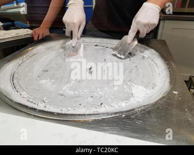 Nahaufnahmen der Hände eines Arbeitnehmers Vorbereitung einer gefrorenen Oberfläche für die Produktion von gewalzten Eis in eine Eisdiele in der Silicon Valley, Mountain View, Kalifornien, 3. Mai 2019. () Stockfoto