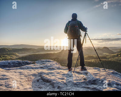 Artist set Kamera und Stativ den Sonnenaufgang Foto auf einem felsigen Gipfel zu. Künstler arbeitet in der Natur Stockfoto