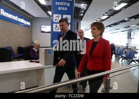 Die erste Ministerin Nicola Sturgeon mit Sir John Elvidge (hinten), dem Vorsitzenden des Flughafens Edinburgh, und dem Vorstandsvorsitzenden Gordon Dewar, während sie bei der offiziellen Eröffnung einer Terminalerweiterung durch den neuen Sitzbereich am Flughafen Edinburgh geht. Millionen £80 wurden in den Ausbau des Terminals investiert, der neue internationale und nationale Ankunftshallen und Gepäckabgabebereiche, neue Gates und Sitzbereiche, neue Flugzeugstände, neue Lounges und neue Einzelhandelsgeschäfte sowie Lebensmittel- und Getränkestände bietet. Stockfoto