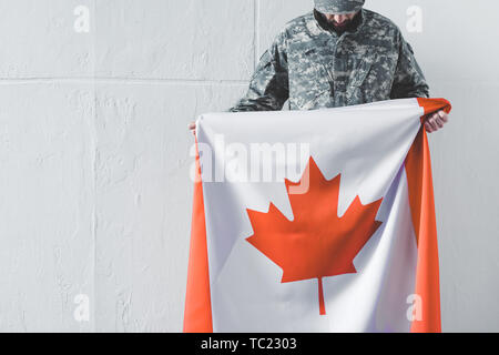 Mann in Uniform holding Kanada Flagge beim Stehen in der Nähe von weißen Wand mit gesenktem Kopf Stockfoto