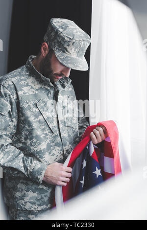 Selektiver Fokus der traurige Mann des Militärs in Uniform Holding usa Nationalflagge, während man durch die Fenster mit gesenktem Kopf Stockfoto