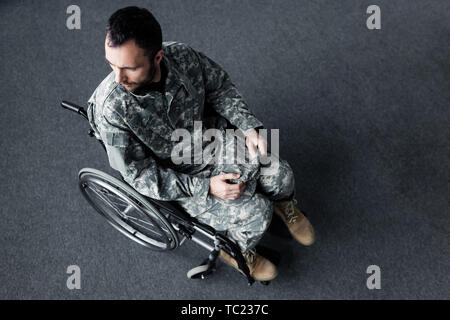 Ansicht von oben behinderter Mann in Uniform sitzt im Rollstuhl und weg schauen Stockfoto