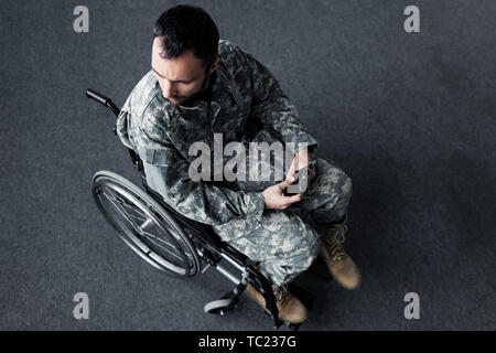 Ansicht von oben behinderter Mann in Uniform sitzt im Rollstuhl und Kappe in der Hand halten Stockfoto