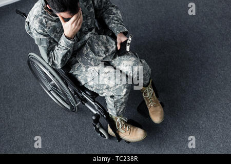 Ansicht von oben der Behinderten militärischen Mann in Uniform sitzen mit Kolben im Rollstuhl und das Gesicht mit der Hand Stockfoto