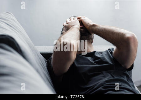 Betätigt man liegt auf dem Sofa und Leiden, während Sie die Hände auf das Gesicht Stockfoto