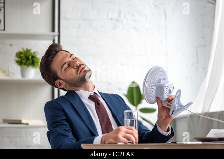 Junge Unternehmer, elektrischer Ventilator, während von der Hitze am Arbeitsplatz leiden Stockfoto