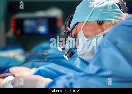 Close up Portrait von weiblichen Chirurg Arzt durch das Tragen von schützender Maske und Hut während der Operation. Gesundheitswesen, medizinische Ausbildung, Chirurgie Konzept. Stockfoto