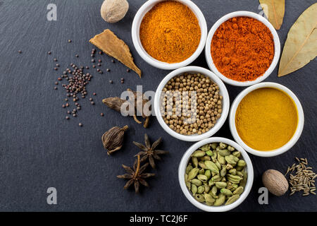 Gewürze in kleinen weißen Schüsseln auf schwarzem Schiefer Hintergrund - Indian Spice Draufsicht Foto mit Platz für Text Stockfoto