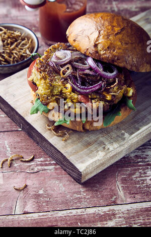 Trendy Bug oder Insekt Burger mit knusprig gebratener Mehlwürmer und Salat Schneiden auf ein frisches knuspriges Brötchen auf einem urigen und Tisch mit Kopie Raum fo serviert. Stockfoto