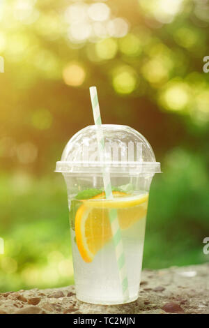 Sommer trinken frische Limonade mit Orange und Minze im Plastikbecher gegen leuchtend grünen Hintergrund. Warme Sonne Flare. Stockfoto